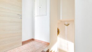 Un pasillo limpio y moderno con una puerta de madera, una pared blanca con un espejo y un suelo de baldosas.