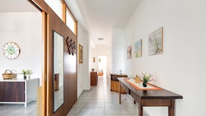 A hallway with a wooden door, a white wall clock, a mirror, and a wooden table with a plant. - 2186 Attico Demetra (Avetrana)