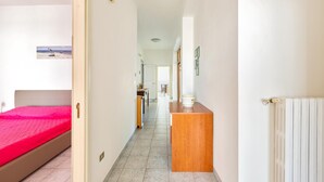 A hotel room with a bed, a wooden nightstand, a radiator, and a hallway leading to a dining area. - 2186 Attico Demetra (Avetrana)