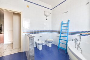 A bathroom with a blue floor, white tiles, a white sink, a toilet, a bathtub, and a blue ladder.