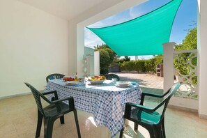 Uma área de refeições com uma mesa posta para dois, coberta por toalha xadrez azul e branca, e uma vela de sombreamento verde suspensa.