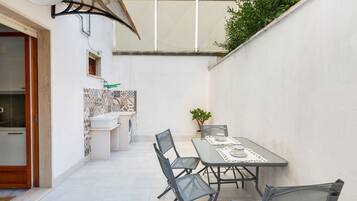 A compact outdoor dining area with a table and chairs, a small potted plant, and a tiled backsplash in the background.