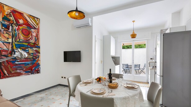 A dining area with a table set for four, a large abstract painting on the wall, and a modern kitchen in the background. - 2150 Casa Mandù (Manduria)