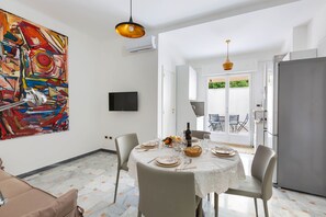 A dining area with a table set for four, a large abstract painting on the wall, and a modern kitchen in the background.