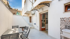 A small outdoor dining area with a table and chairs, a staircase leading to an upper level, and a kitchen visible through an open door. - 2150 Casa Mandù (Manduria)