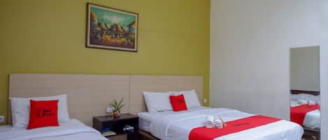 A hotel room with two beds, each with a red and white bedspread, a painting on the wall, and a nightstand with a plant.