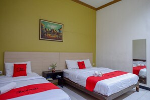 A hotel room with two beds, each with a red and white bedspread, a painting on the wall, and a nightstand with a plant. - Reddoorz Plus @ Hotel Asih UNY (Depok)