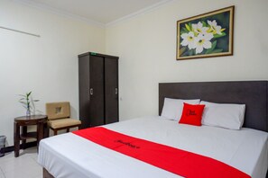A hotel room with a bed, a chair, a small table, a wardrobe, and a painting on the wall. - Reddoorz Plus @ Hotel Asih UNY (Depok)