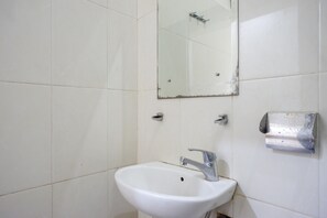 A bathroom with a white sink, a mirror, and a soap dispenser on the wall. - Reddoorz Plus @ Hotel Asih UNY (Depok)