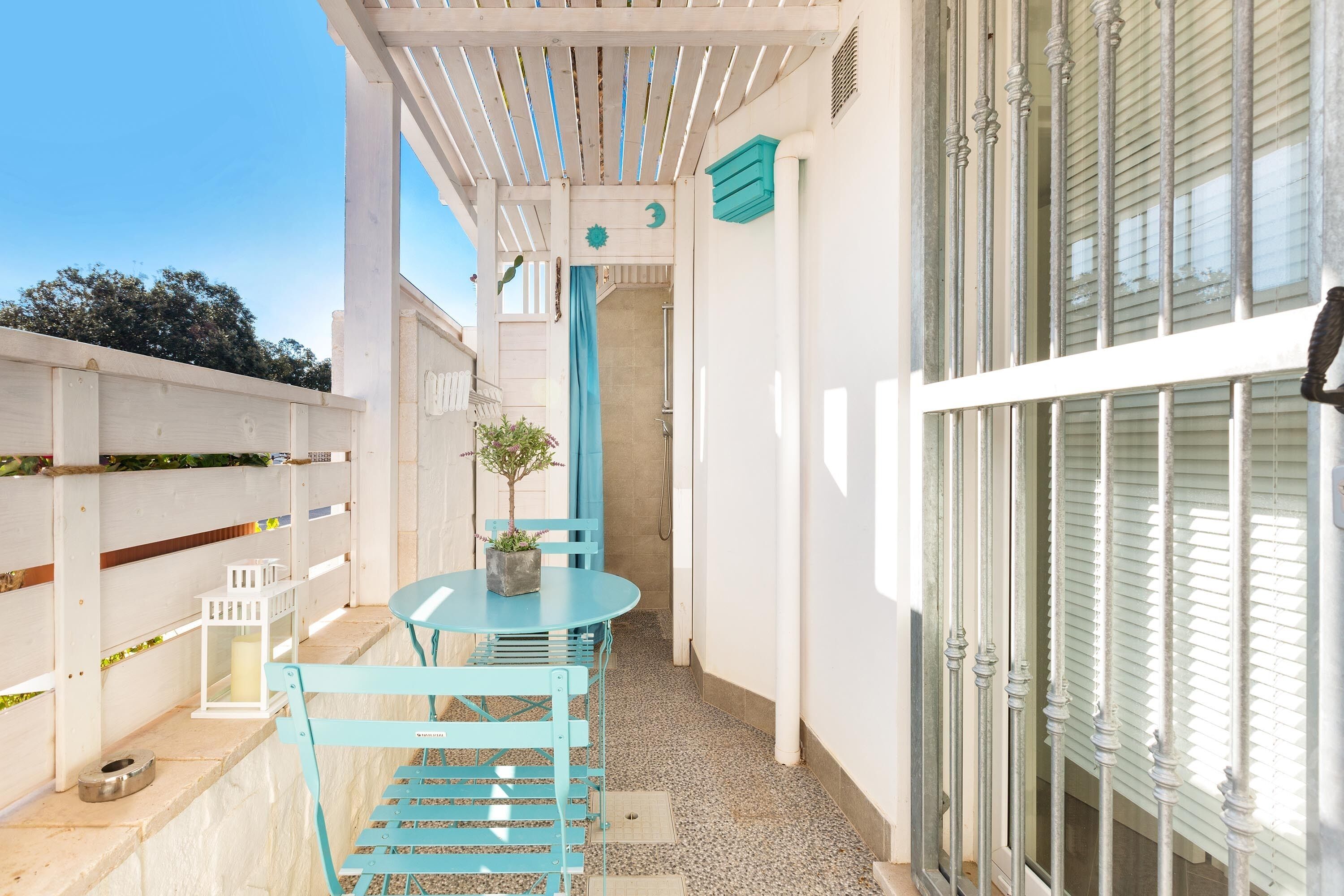 A small patio area with a round table and two chairs, a potted plant, and a white lantern.