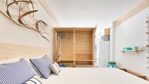 Un dormitorio con una cama, almohadas, un armario de madera y un pequeño taburete.