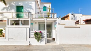 Un edificio blanco con balcón, una puerta verde y un pequeño jardín con flores.