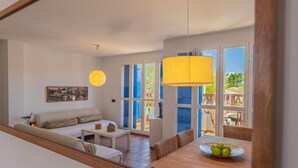 A spacious living area with a sofa, dining table, and a view through large windows.