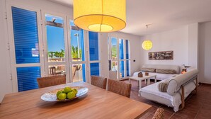 A room with a wooden dining table, wicker chairs, a sofa, and a hanging lamp.