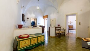 A hallway with a green and yellow cabinet, a wooden chair, and a tiled floor. - 2163 Palazzo Grassi (Martina Franca)
