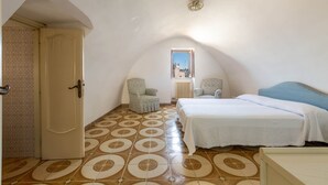 A bedroom with a sloped ceiling, two beds, a small window, and patterned floor tiles. - 2163 Palazzo Grassi (Martina Franca)