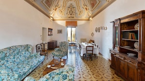 A spacious living room with a patterned floor, a sofa, a wooden cabinet, and a dining area with a table and chairs. - 2163 Palazzo Grassi (Martina Franca)