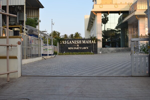 La entrada al Sri Ganesh Mahal y Mini Party Lawn, con un camino pavimentado y un letrero grande.