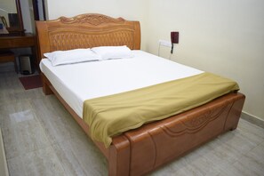 Una cama bien tendida con cabecera de madera, una mesita de noche y un cesto de basura.