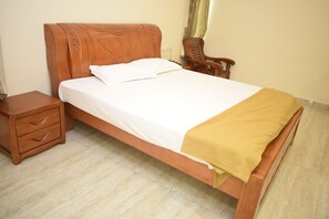 Una cama individual con cabecera de madera, una mesita de noche con cajones y una silla.