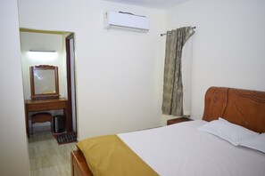 Una habitación de hotel con cama, un escritorio de madera con espejo, aire acondicionado y una cortina.