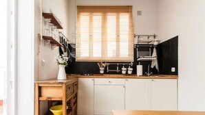 A compact kitchen with white cabinets, a wooden countertop, and a window with blinds. - Alohamundi San Diego (Sevilla)