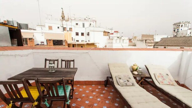 A rooftop terrace with a table and chairs, a sunbed, and a view of the cityscape. - Alohamundi San Diego (Sevilla)