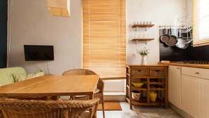 A compact kitchen with a dining area, featuring a wooden table, wicker chairs, and a built-in stove. - Alohamundi San Diego (Sevilla)