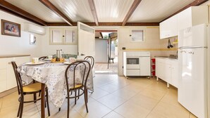 Un coin repas avec une table dressée pour quatre personnes, une cuisine avec des appareils électroménagers blancs et un plafond orné de poutres en bois.