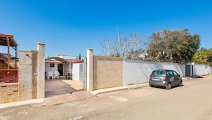 Un quartier résidentiel avec une allée pavée, une voiture garée et un bâtiment doté d’un mur en pierre et d’un patio couvert.