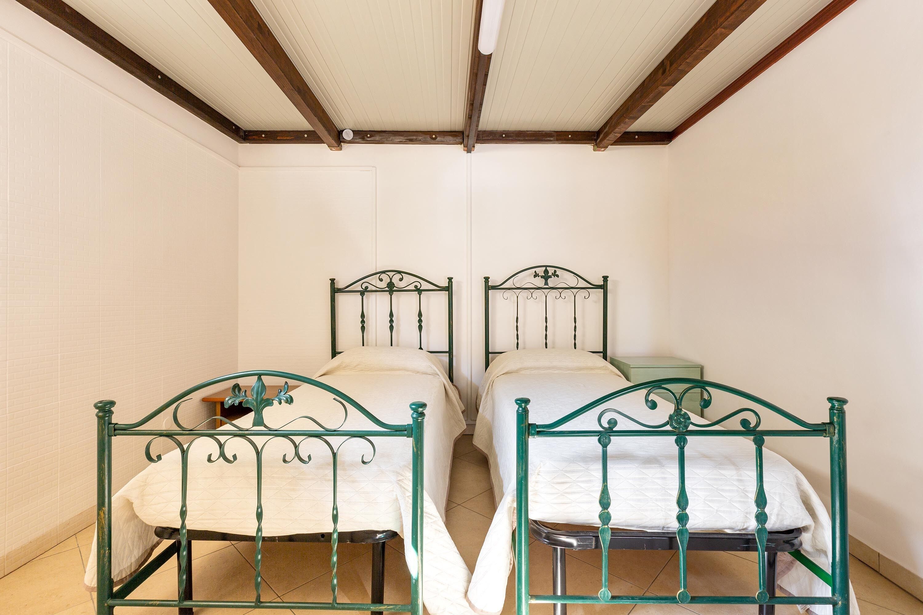 A room with two metal beds with white bedding, wooden beams on the ceiling, and white walls.