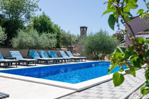 A swimming pool with lounge chairs, surrounded by greenery and a stone tower.