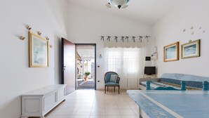 A spacious room with a large bed, a chair, and a bench. There is a door leading to another room, and a window with curtains. - 2299 Villetta Noemi (Porto Cesareo)