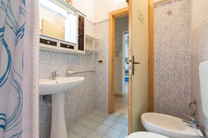 A bathroom with a white sink, a mirror above it, and a shower area with a tiled wall.