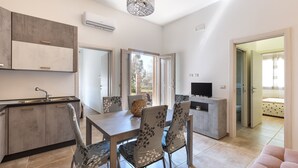 Een moderne keuken met een eetgedeelte, een televisie en een slaapkamer zichtbaar door een open deur.