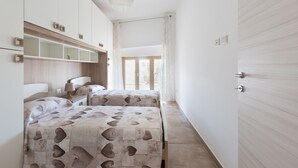 Een slaapkamer met twee bedden, een nachtkastje met lamp, een kledingkast en een raam met gordijnen.