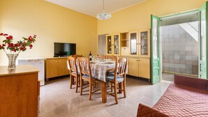 Un coin repas avec une table dressée pour quatre personnes, des chaises en bois, un téléviseur et un vase rempli de fleurs rouges.