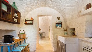 Una cocina rústica con paredes de piedra, una mesa de madera con taburetes y un arco de piedra que conduce a otra habitación.