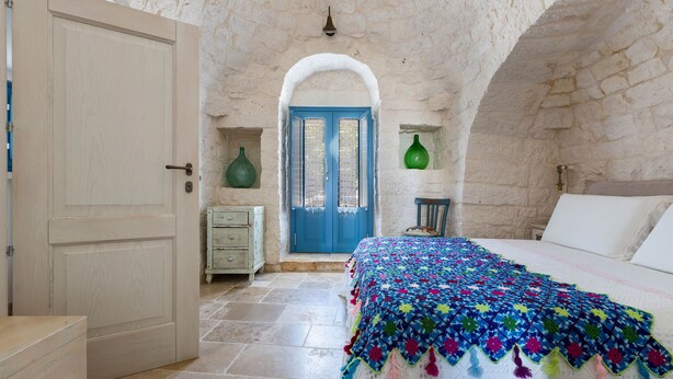 Un dormitorio con cama, una puerta, un aparador y una pared de piedra.
