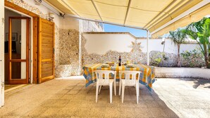 An outdoor patio with a table and chairs, a wooden door, and a stone wall. - 2019 Villetta del Colle (Porto Cesareo)