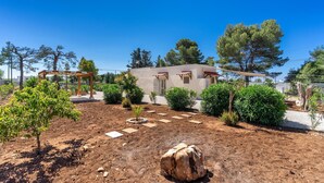 Une maison avec un jardin, une pergola et un grand arbre.