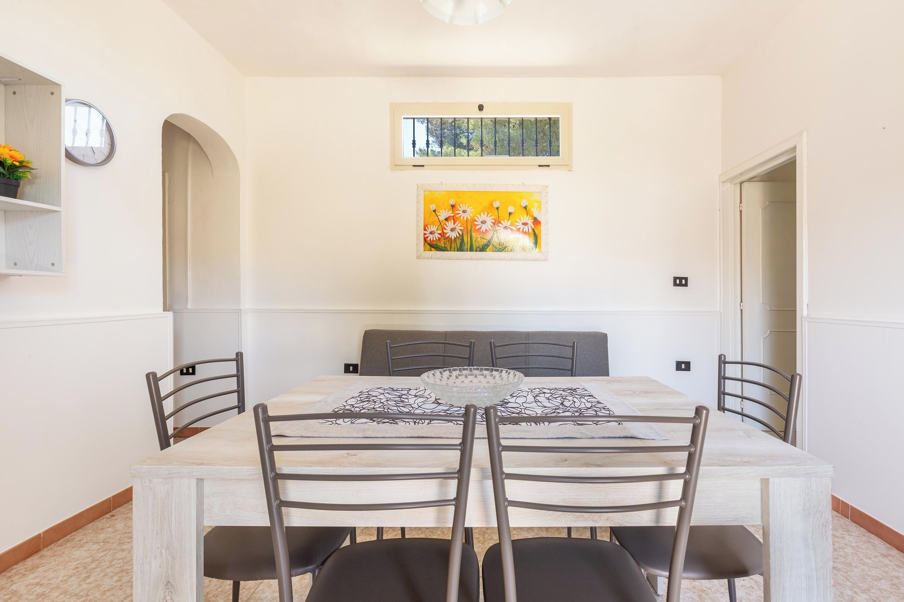 A dining area with a rectangular table, four chairs, a glass bowl, and two wall-mounted paintings.