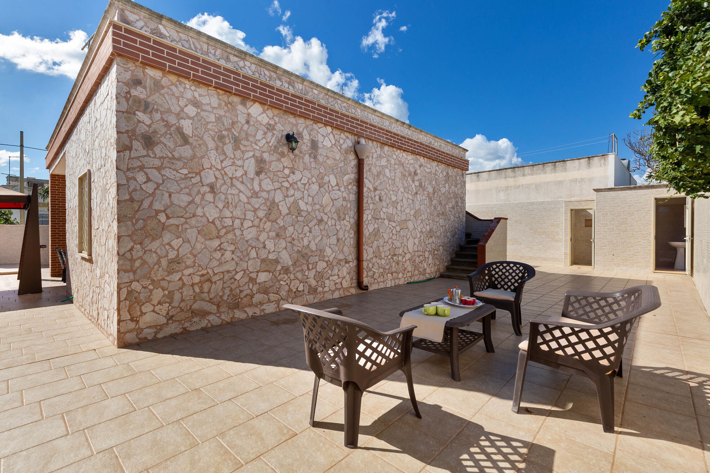 An outdoor patio with a stone wall, a table, and two chairs.