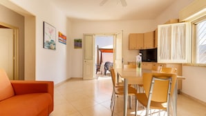 A modern kitchen with a dining table, chairs, and a TV. There is a sofa and a door leading to a balcony. - 2100 Villetta Martina (Porto Cesareo)