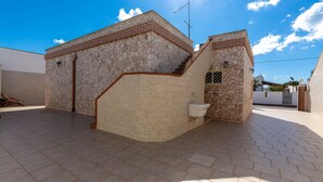 A building with a stone exterior, a small attached structure, and a tiled patio area. - 2100 Villetta Martina (Porto Cesareo)