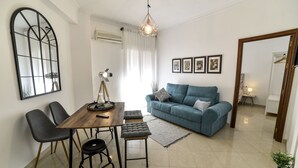 A modern living room with a blue sofa, a wooden dining table with chairs, a hanging light fixture, and framed pictures on the wall. - Alohamundi San Leandro (Sevilla)