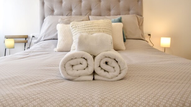 A neatly made bed with rolled towels, a tufted headboard, and patterned bedding. - Alohamundi San Leandro (Sevilla)