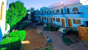 A courtyard with a row of buildings, a tree, and a crescent moon in the sky. - Happy Land Hotel (Dahab)