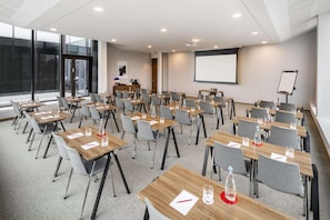Una sala de conferencias con varias mesas y sillas, una pantalla de proyector y una pizarra.