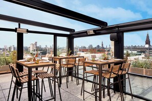 An outdoor dining area with tables and chairs, large windows offering a city view, and a pergola structure. - NH Collection Copenhagen (Copenhagen)